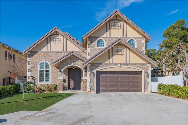 tudor home with a garage, fence, driveway, stucco siding, and a front lawn