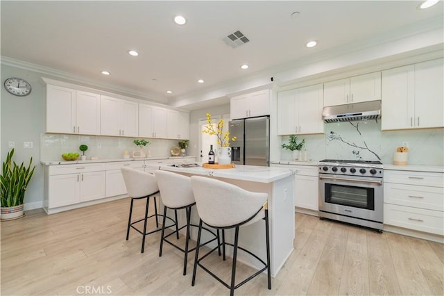 kitchen with under cabinet range hood, light countertops, appliances with stainless steel finishes, light wood-type flooring, and crown molding