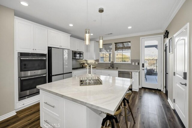 kitchen with stainless steel appliances, a kitchen island, hanging light fixtures, and white cabinets