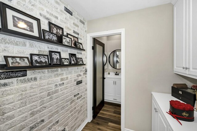 hall with brick wall, dark hardwood / wood-style flooring, and sink