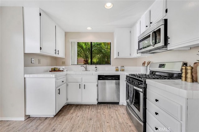 kitchen with stainless steel appliances, light hardwood / wood-style floors, white cabinetry, and tile counters