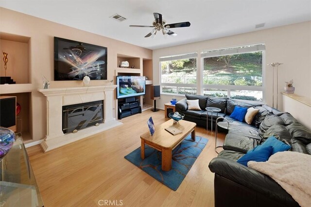 living room with ceiling fan, built in features, and light wood-type flooring