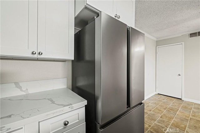 kitchen featuring white cabinetry, stainless steel fridge, light stone countertops, and a textured ceiling