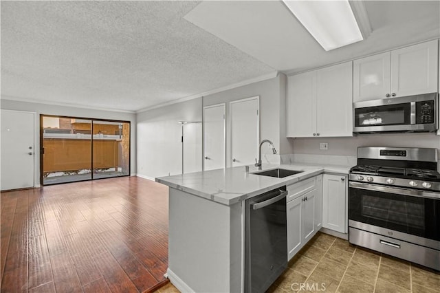 kitchen with white cabinetry, sink, stainless steel appliances, and kitchen peninsula