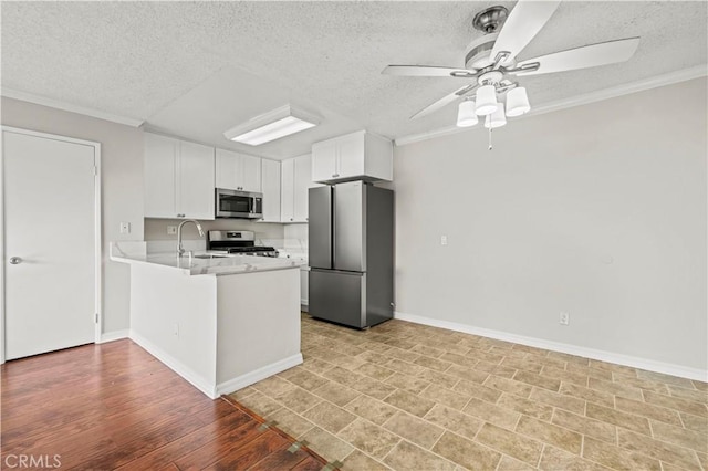 kitchen with appliances with stainless steel finishes, sink, white cabinets, ornamental molding, and kitchen peninsula