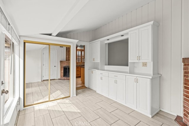 kitchen with white cabinets, a fireplace, and vaulted ceiling with beams