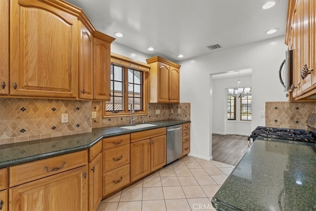 kitchen featuring light tile patterned floors, stainless steel appliances, a notable chandelier, dark stone counters, and sink