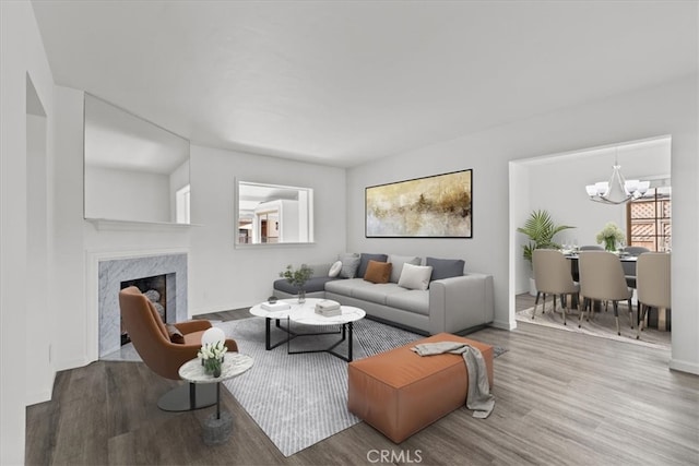 living room with a high end fireplace, baseboards, an inviting chandelier, and wood finished floors