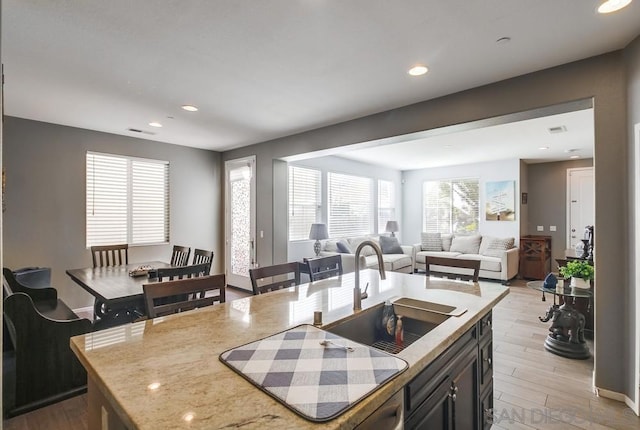 kitchen with a kitchen island with sink, light stone countertops, sink, and light hardwood / wood-style floors