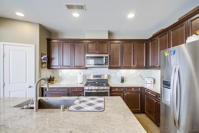 kitchen with stainless steel appliances, sink, tasteful backsplash, and light stone countertops