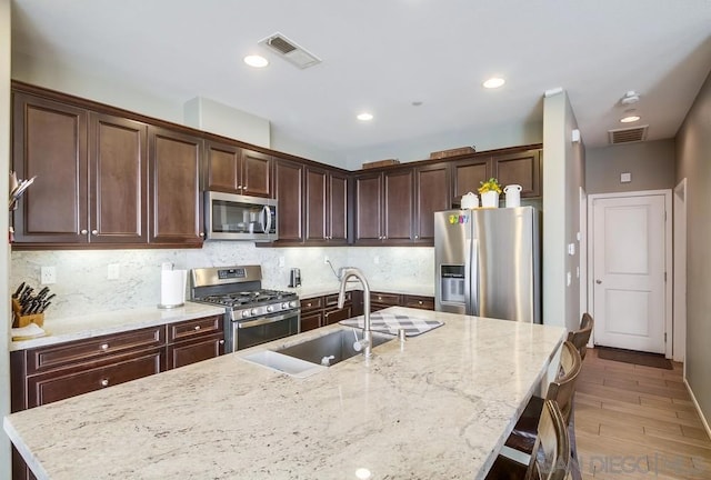 kitchen with backsplash, sink, light stone countertops, a breakfast bar area, and stainless steel appliances