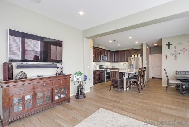 interior space with light hardwood / wood-style floors, dark brown cabinetry, a kitchen island with sink, appliances with stainless steel finishes, and a breakfast bar area