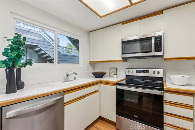 kitchen with stainless steel appliances, light hardwood / wood-style floors, white cabinetry, and sink