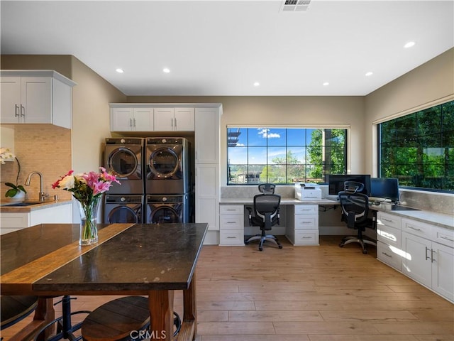 home office featuring stacked washing maching and dryer, built in desk, light hardwood / wood-style floors, and sink