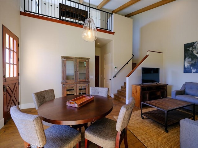 dining area featuring a high ceiling, beam ceiling, and light wood-type flooring