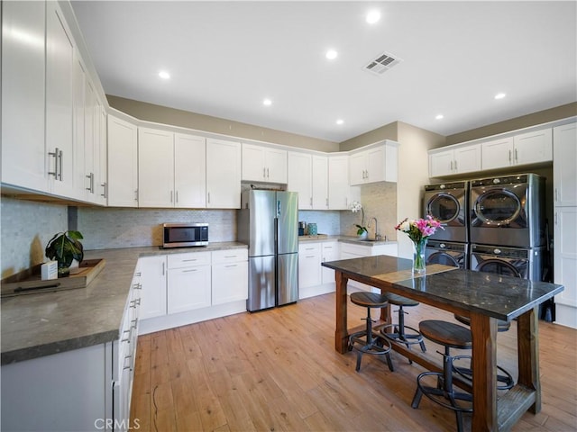 kitchen with stacked washer / drying machine, light wood-type flooring, stainless steel appliances, and white cabinetry