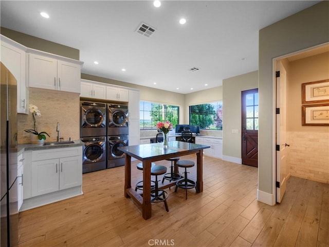 kitchen with sink, white cabinetry, stacked washer / drying machine, and light hardwood / wood-style flooring