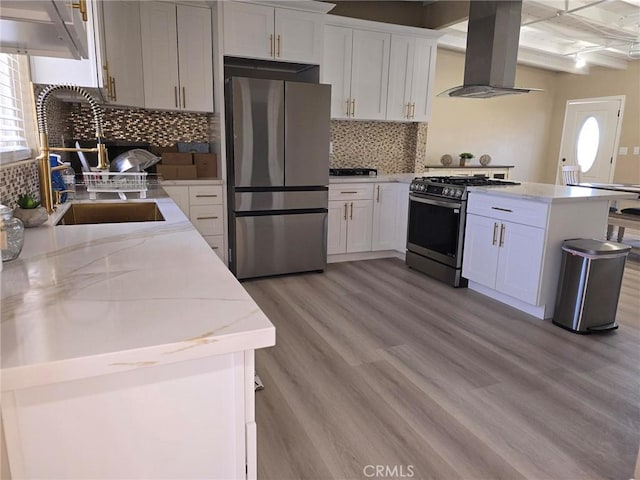 kitchen featuring white cabinetry, island exhaust hood, appliances with stainless steel finishes, light wood-type flooring, and light stone counters