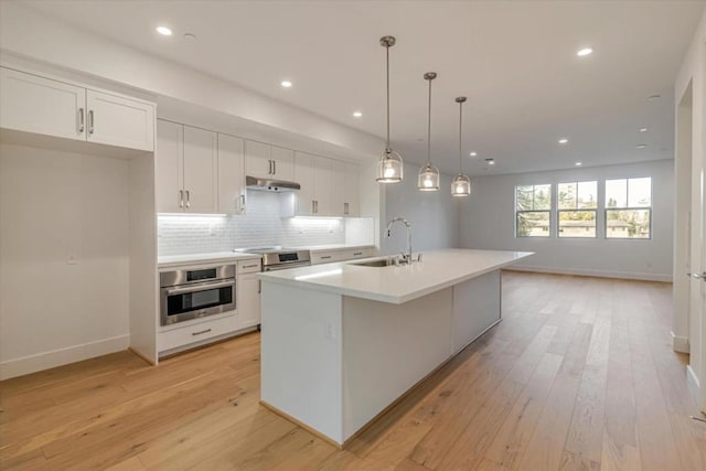 kitchen with white cabinetry, a center island with sink, stainless steel oven, hanging light fixtures, and sink