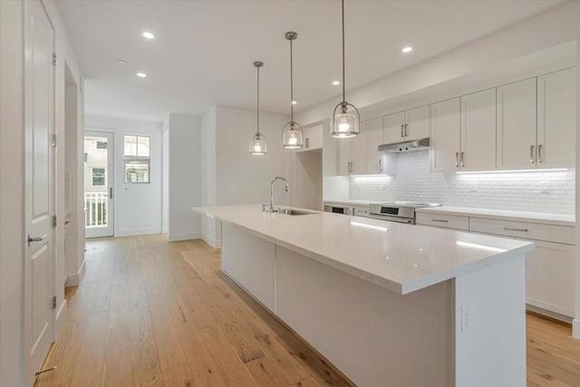 kitchen featuring tasteful backsplash, sink, white cabinetry, hanging light fixtures, and a kitchen island with sink