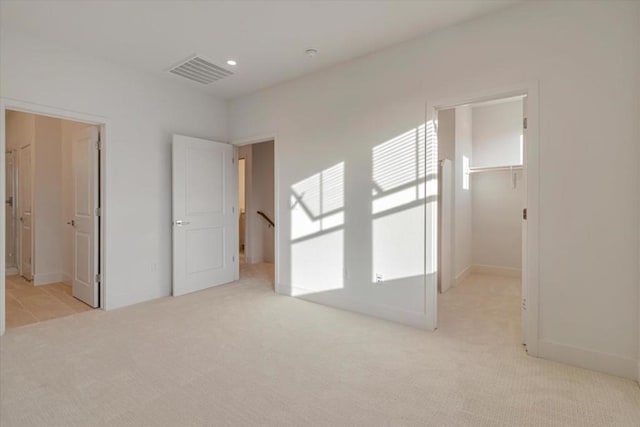 unfurnished bedroom featuring ensuite bathroom, a walk in closet, a closet, and light colored carpet