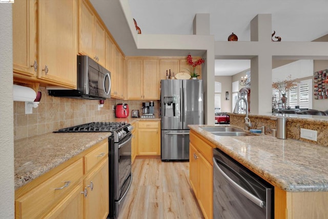 kitchen with light stone countertops, appliances with stainless steel finishes, light brown cabinetry, sink, and a notable chandelier