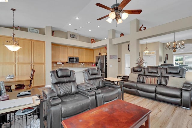 living room featuring high vaulted ceiling, ceiling fan with notable chandelier, and light hardwood / wood-style flooring