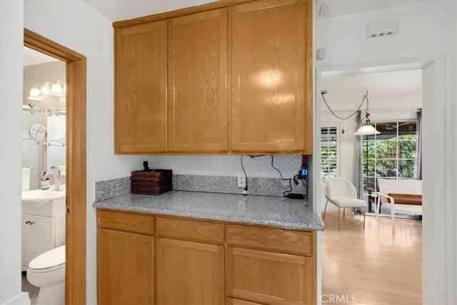 kitchen with light stone countertops, sink, light wood-type flooring, and decorative backsplash