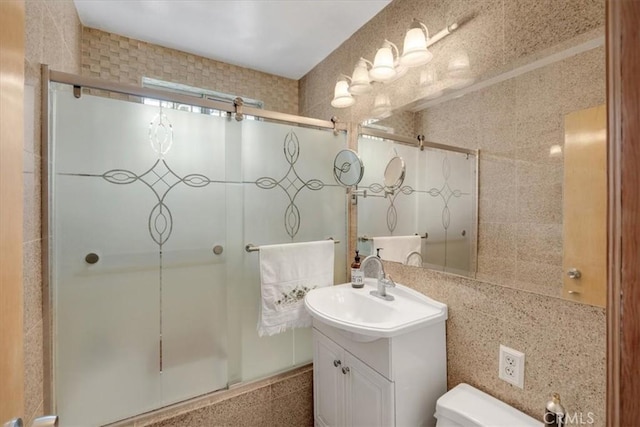 full bathroom featuring toilet, shower / bath combination with glass door, tile walls, vanity, and backsplash