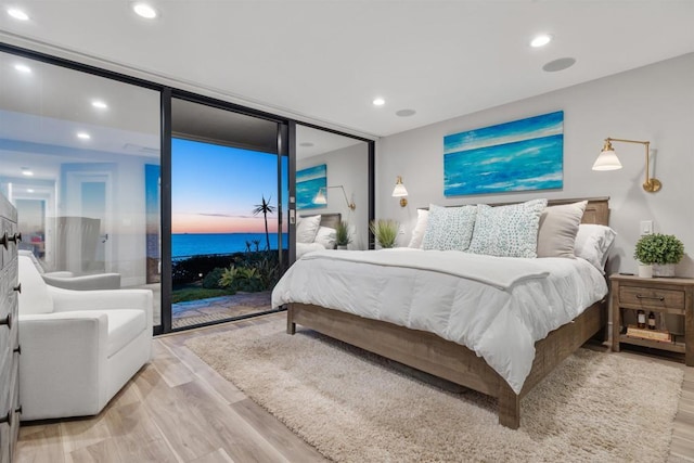 bedroom featuring a water view, expansive windows, access to exterior, and light wood-type flooring