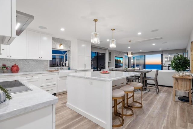 kitchen featuring pendant lighting, a kitchen island, sink, white cabinets, and black electric cooktop