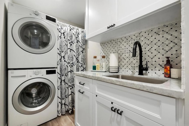 washroom with stacked washer and dryer, cabinets, light hardwood / wood-style floors, and sink