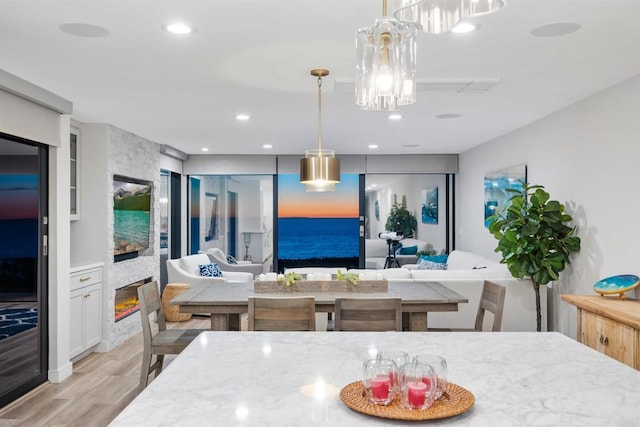 kitchen with pendant lighting, white cabinets, a stone fireplace, and light wood-type flooring