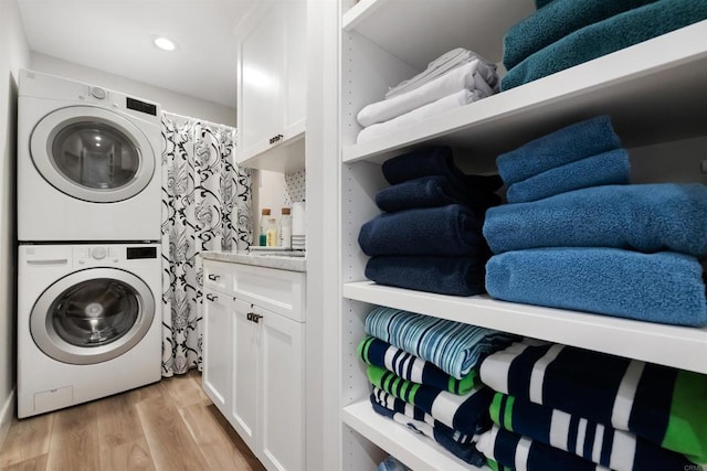 washroom with cabinets, light hardwood / wood-style flooring, and stacked washer and dryer