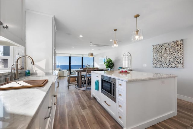 kitchen featuring decorative light fixtures, white cabinetry, stainless steel microwave, and a kitchen island