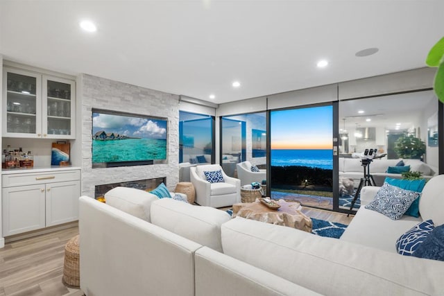 living room featuring a water view, light wood-type flooring, and a stone fireplace