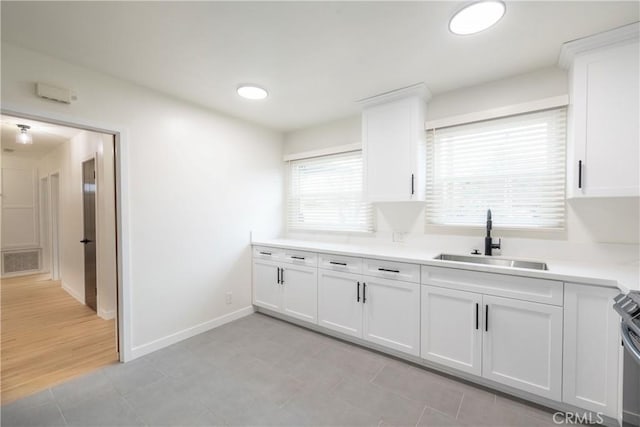 kitchen with light tile patterned floors, sink, white cabinets, and range