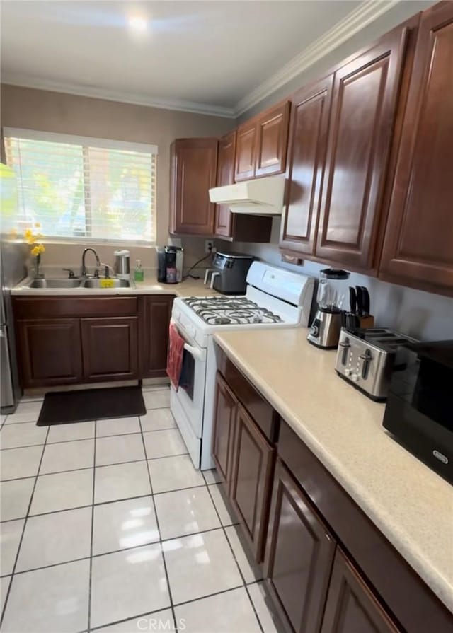 kitchen featuring crown molding, gas range gas stove, light countertops, a sink, and under cabinet range hood