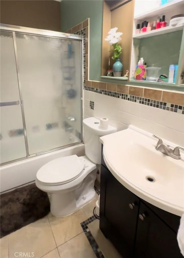 full bathroom with decorative backsplash, bath / shower combo with glass door, vanity, tile patterned flooring, and toilet