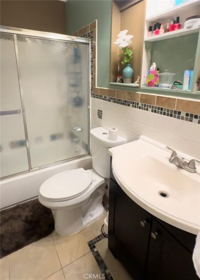 bathroom with tile walls, bath / shower combo with glass door, toilet, vanity, and tile patterned flooring