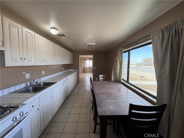 kitchen featuring sink, light tile patterned flooring, white gas range, tile counters, and white cabinets