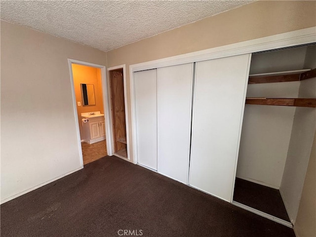 unfurnished bedroom featuring a closet, sink, a textured ceiling, and dark colored carpet