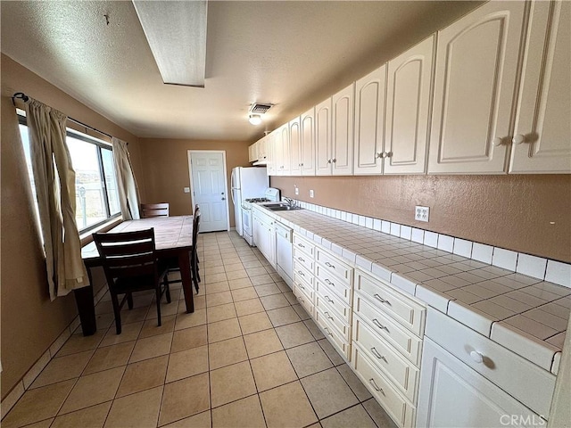 kitchen with white appliances, tile counters, white cabinetry, sink, and light tile patterned floors