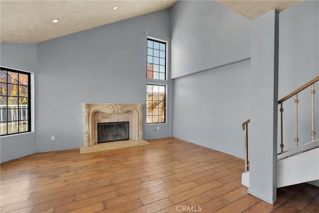 unfurnished living room featuring a high end fireplace, a towering ceiling, and light hardwood / wood-style floors