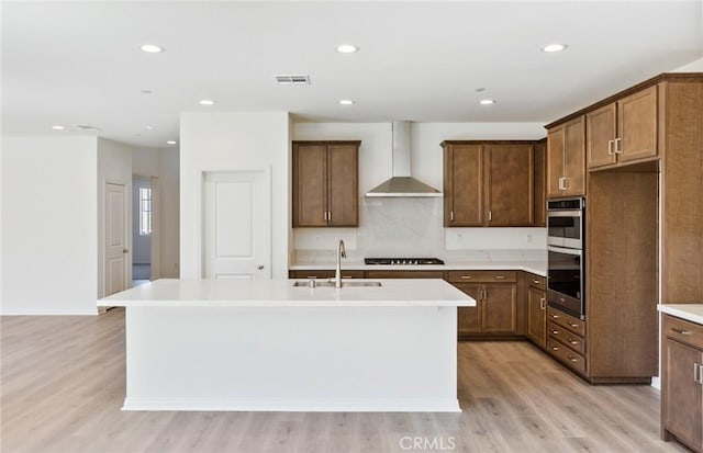 kitchen featuring wall chimney exhaust hood, sink, a center island with sink, and light hardwood / wood-style flooring