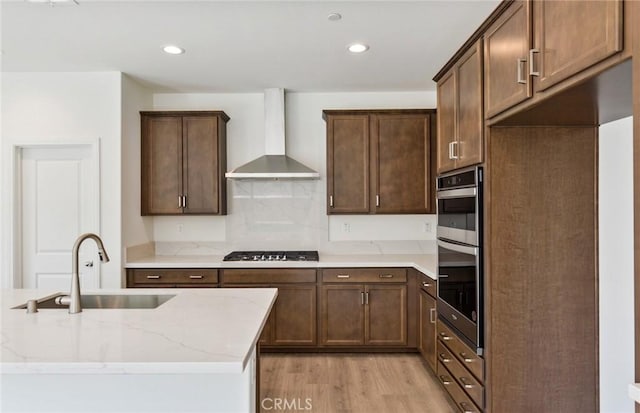 kitchen featuring light stone counters, sink, wall chimney exhaust hood, and light wood-type flooring