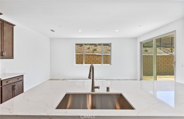 kitchen featuring light stone countertops, sink, and dark brown cabinets