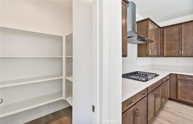 kitchen with stainless steel gas stovetop, wall chimney range hood, dark brown cabinetry, and light hardwood / wood-style flooring