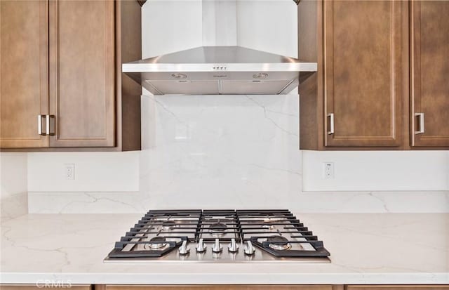 kitchen with tasteful backsplash, stainless steel gas stovetop, light stone countertops, and wall chimney exhaust hood