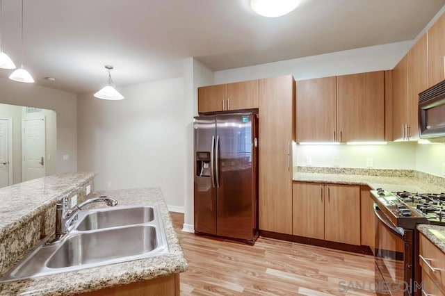 kitchen featuring pendant lighting, stainless steel refrigerator with ice dispenser, sink, light wood-type flooring, and black gas range oven